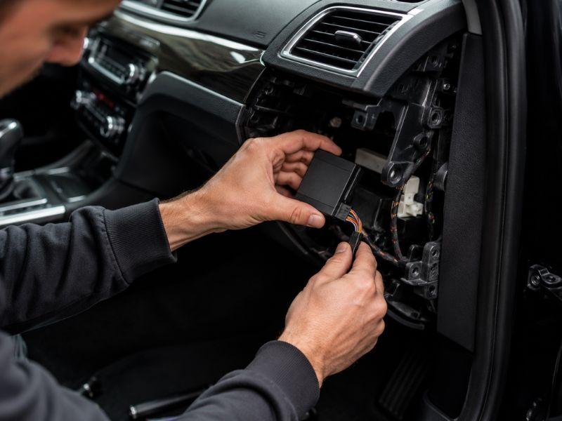 Professional technician hardwiring a concealed GPS tracking device behind a car dashboard
