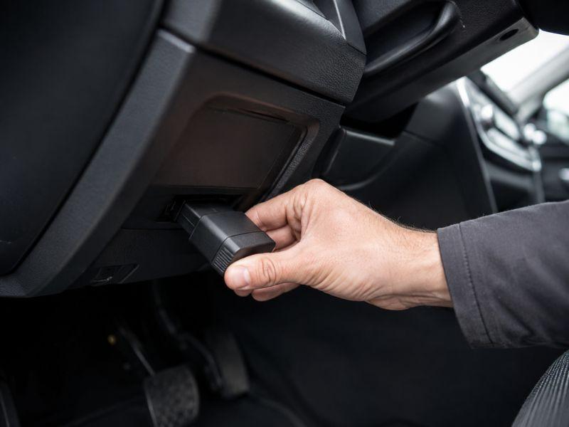 Hand plugging a GPS OBD tracker into a vehicle OBD port